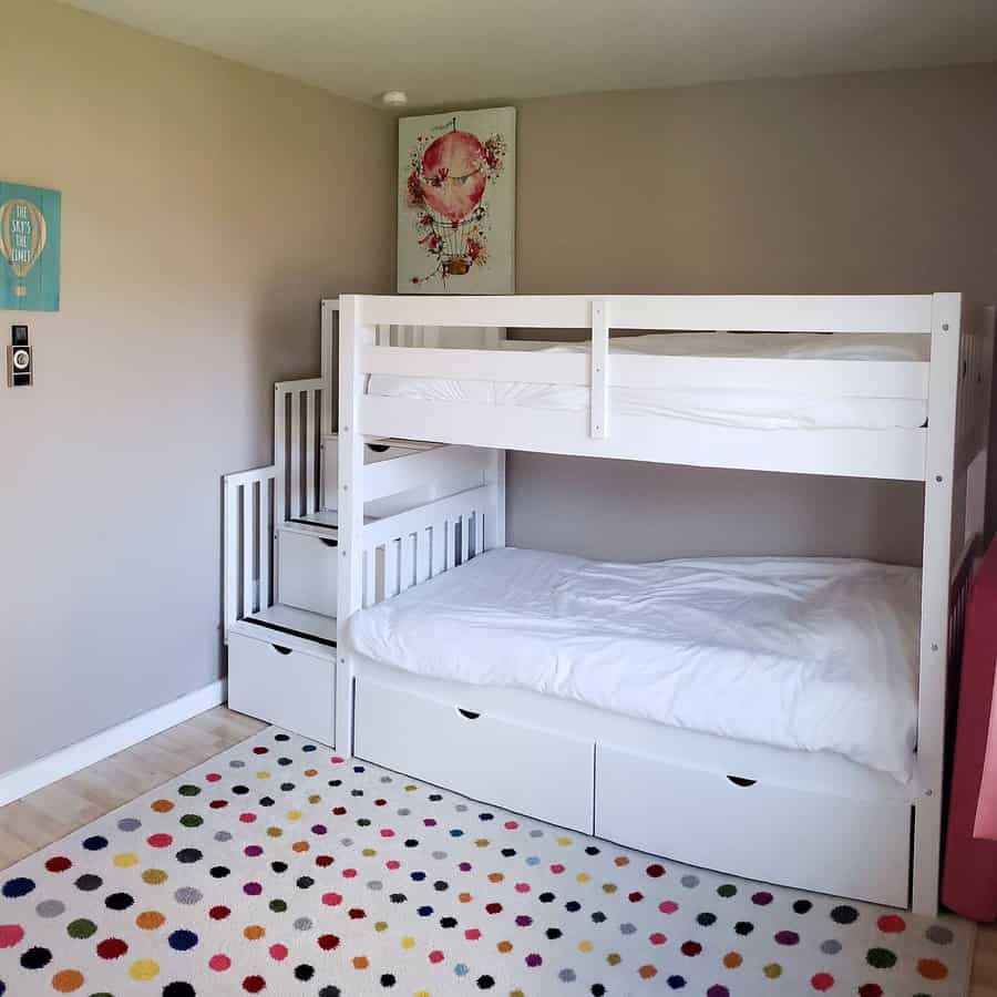 Children's room with a white bunk bed, polka dot rug, and wall art; stairs with storage lead to the top bunk