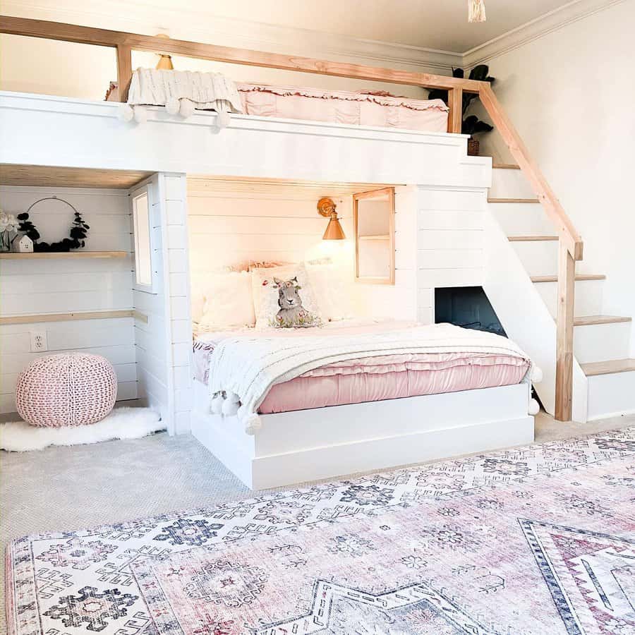 Boho bedroom with a white bunk bed and ladder, pink accents, decorative pillows, and a patterned rug on the floor