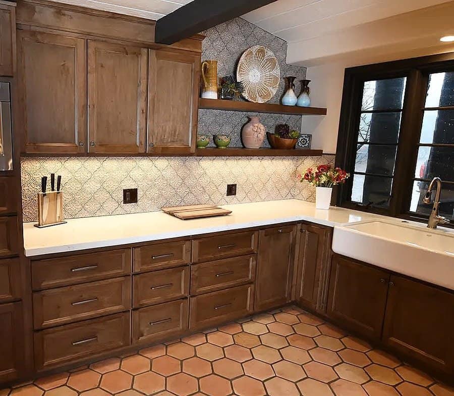 Hexagonal terracotta tile flooring enhances this rustic kitchen, complementing rich wood cabinetry, warm lighting, and decorative tile backsplash