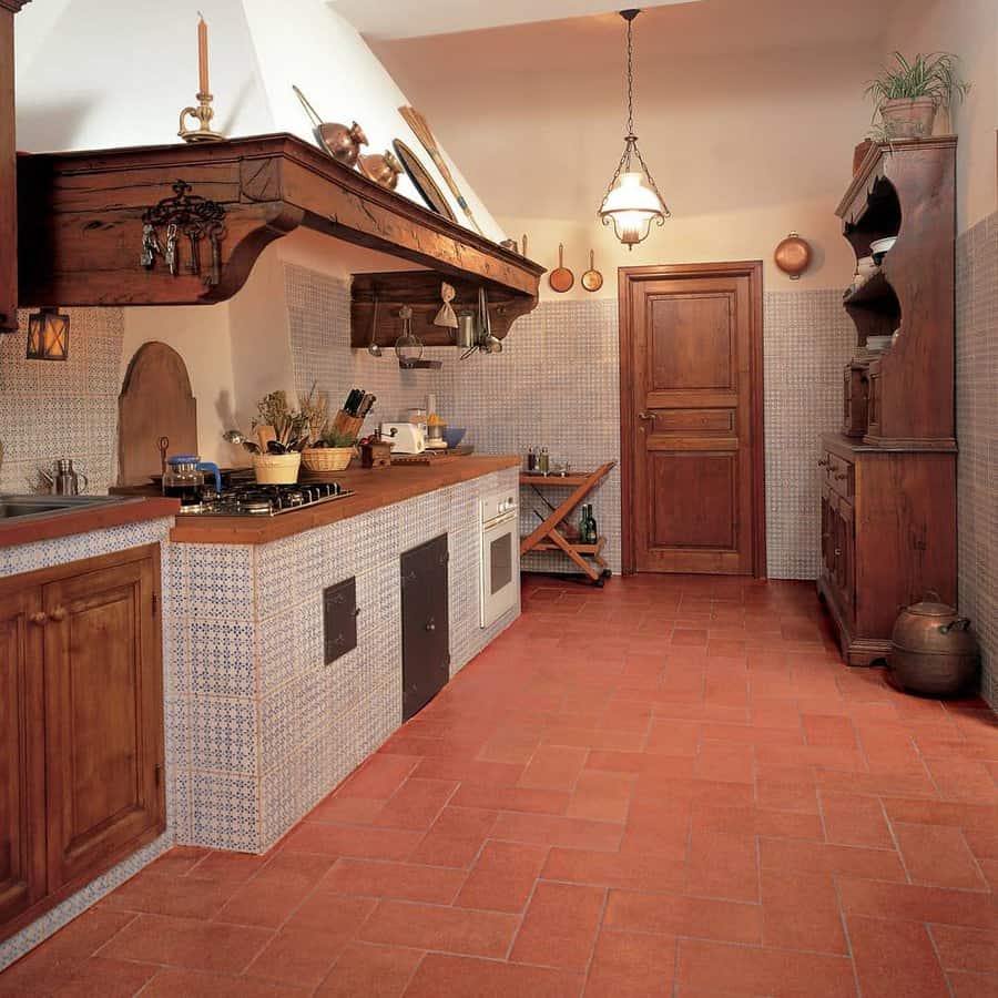 Rustic kitchen with terra cotta tile floor, wooden cabinets, hanging pots, a wooden shelf, and a central wooden door