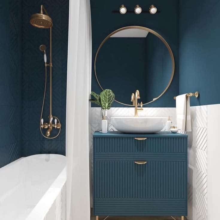 Sophisticated bathroom with deep teal walls, white textured tile backsplash, gold fixtures, round mirror, and a modern vessel sink.