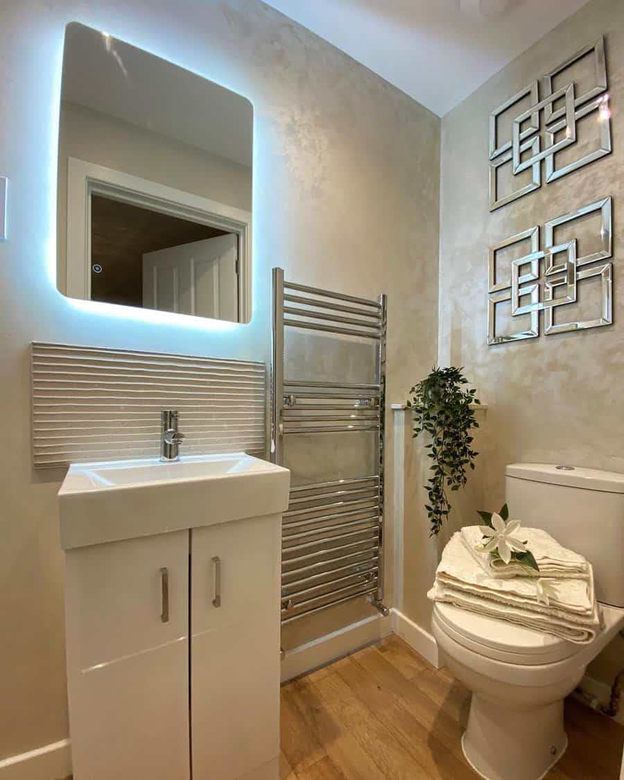 Contemporary bathroom with ribbed white backsplash, backlit mirror, chrome towel warmer, and soft gold textured walls for a sleek spa vibe.