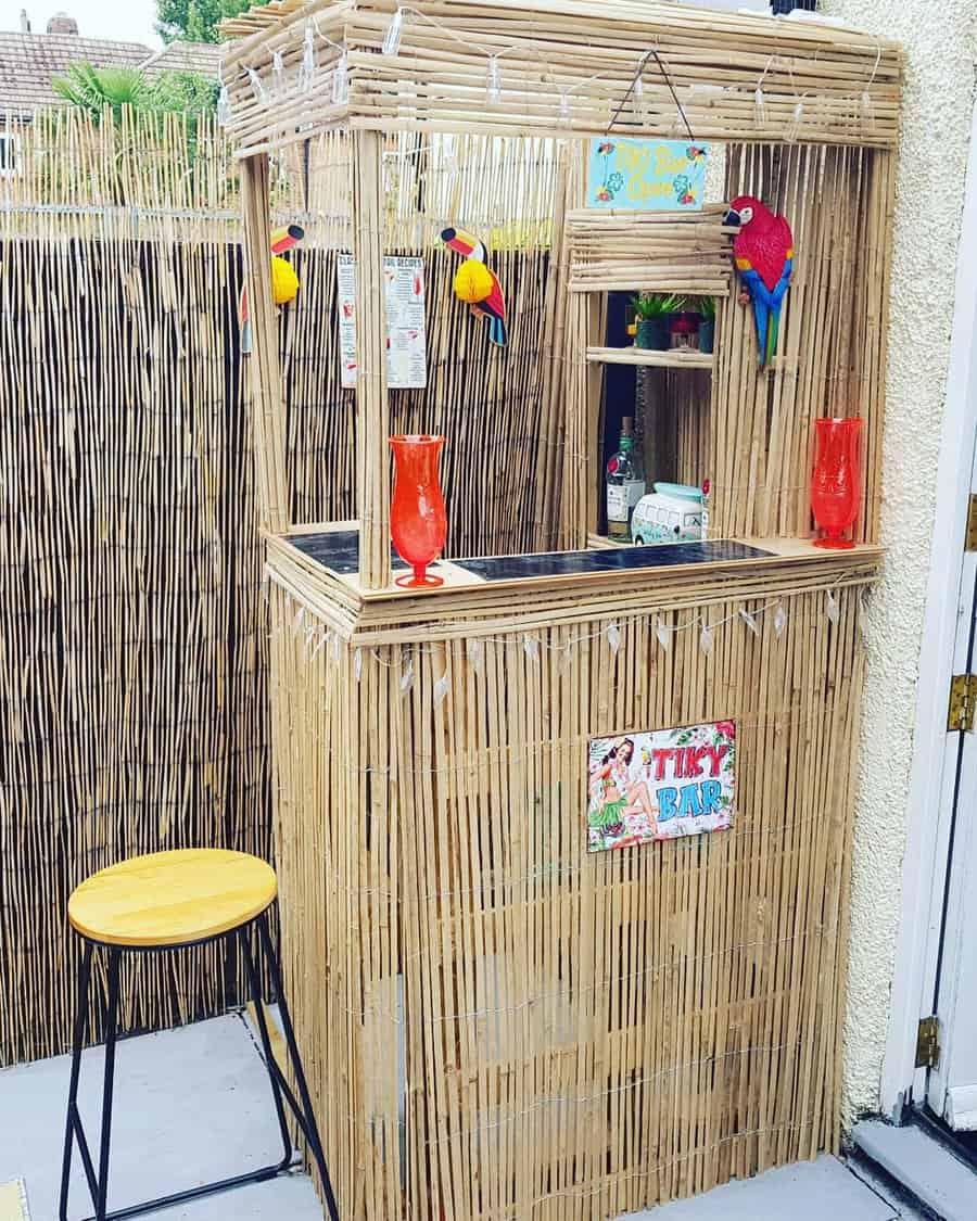 Outdoor tiki bar with bamboo structure, barstool, colorful parrots, and two red tropical drinks decorated with vibrant signs