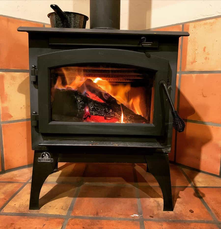 Cozy wood stove set against a terracotta tile hearth, radiating warmth with a crackling fire and rustic charm.