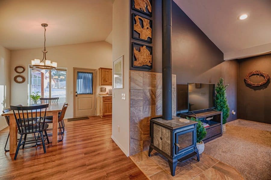 Freestanding wood stove on a tiled hearth, nestled between a cozy living room and dining area, adding warmth and rustic charm to the space.