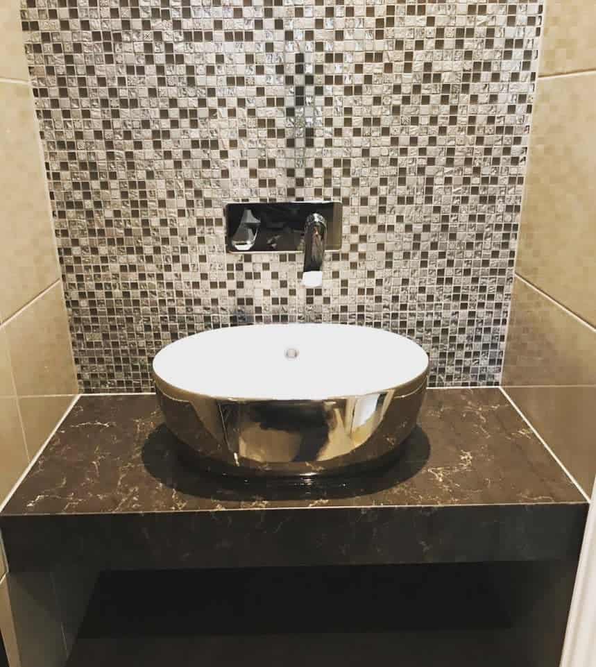 Luxurious bathroom with metallic mosaic tile backsplash, round chrome vessel sink, wall-mounted faucet, and black marble vanity.