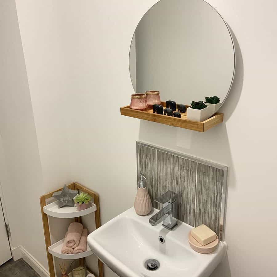 Minimalist bathroom with vertical wood-look tile backsplash, compact white sink, round mirror with shelf, and soft pink and natural decor.