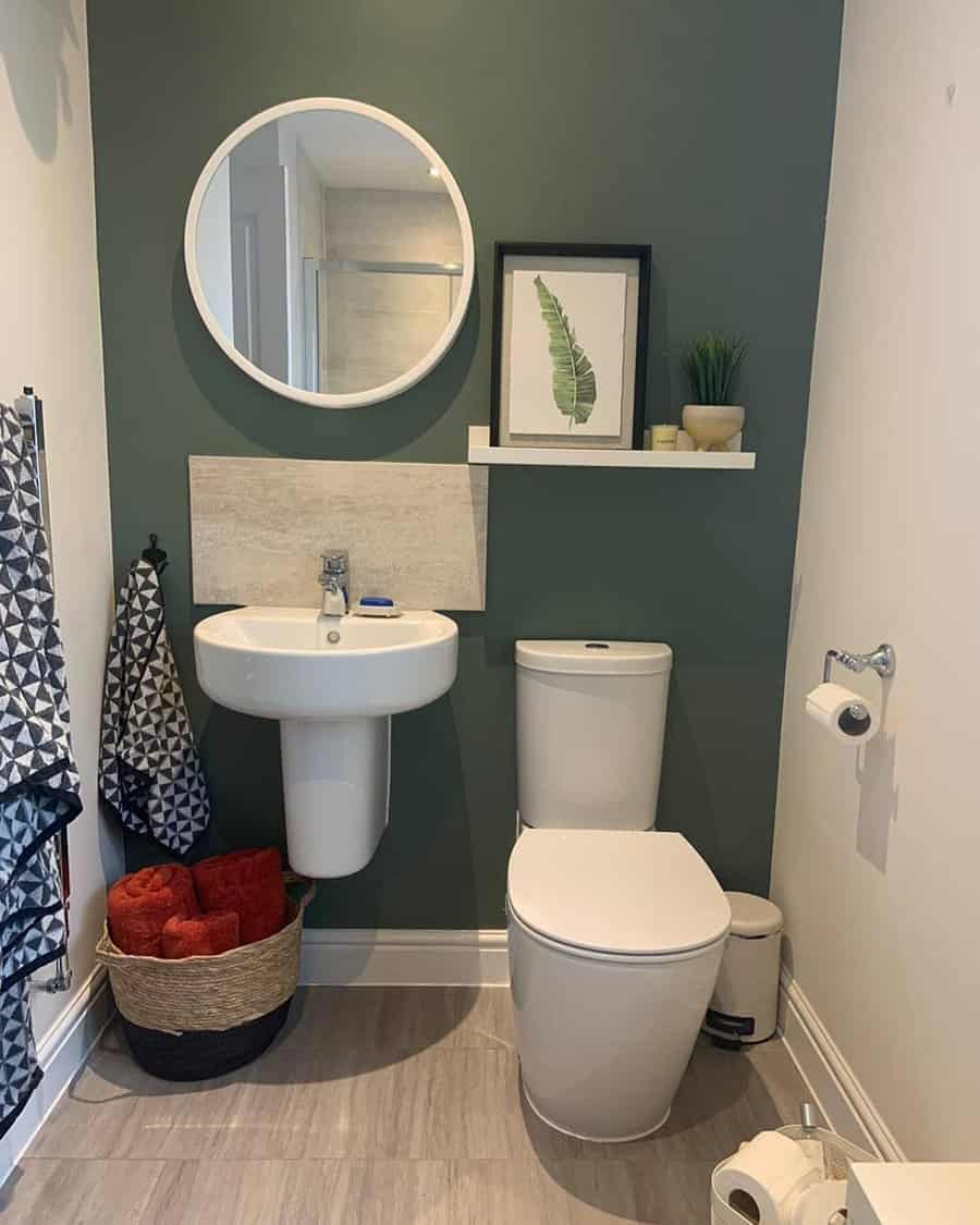 Modern bathroom with minimalist beige tile backsplash, forest green accent wall, round mirror, and sleek white pedestal sink.