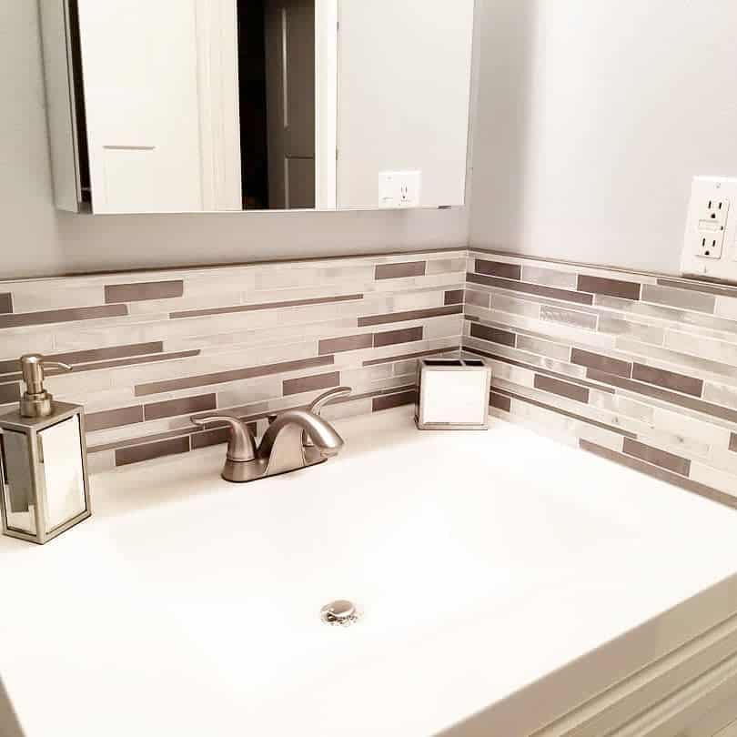 Sleek bathroom with horizontal mosaic tile backsplash in neutral tones, white countertop, and brushed nickel faucet and accessories.