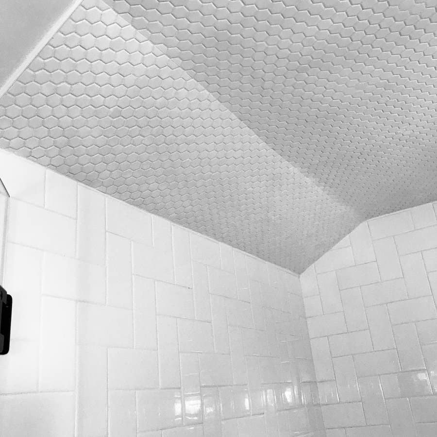 Modern shower with a white hexagonal tile ceiling and herringbone subway tile walls, creating a sleek and cohesive monochrome design.