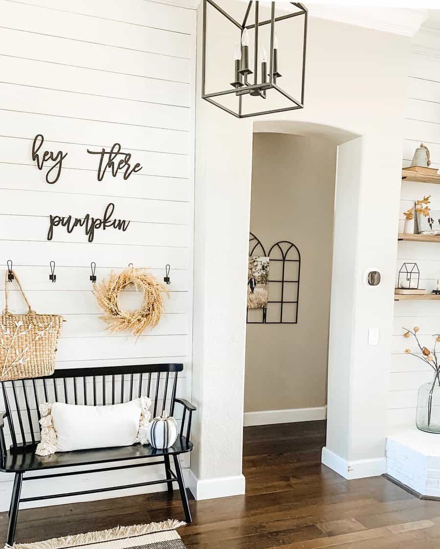 Stylish entryway with a black bench, pumpkin sign, wreath, and modern decor on white shiplap walls creating a warm, inviting atmosphere