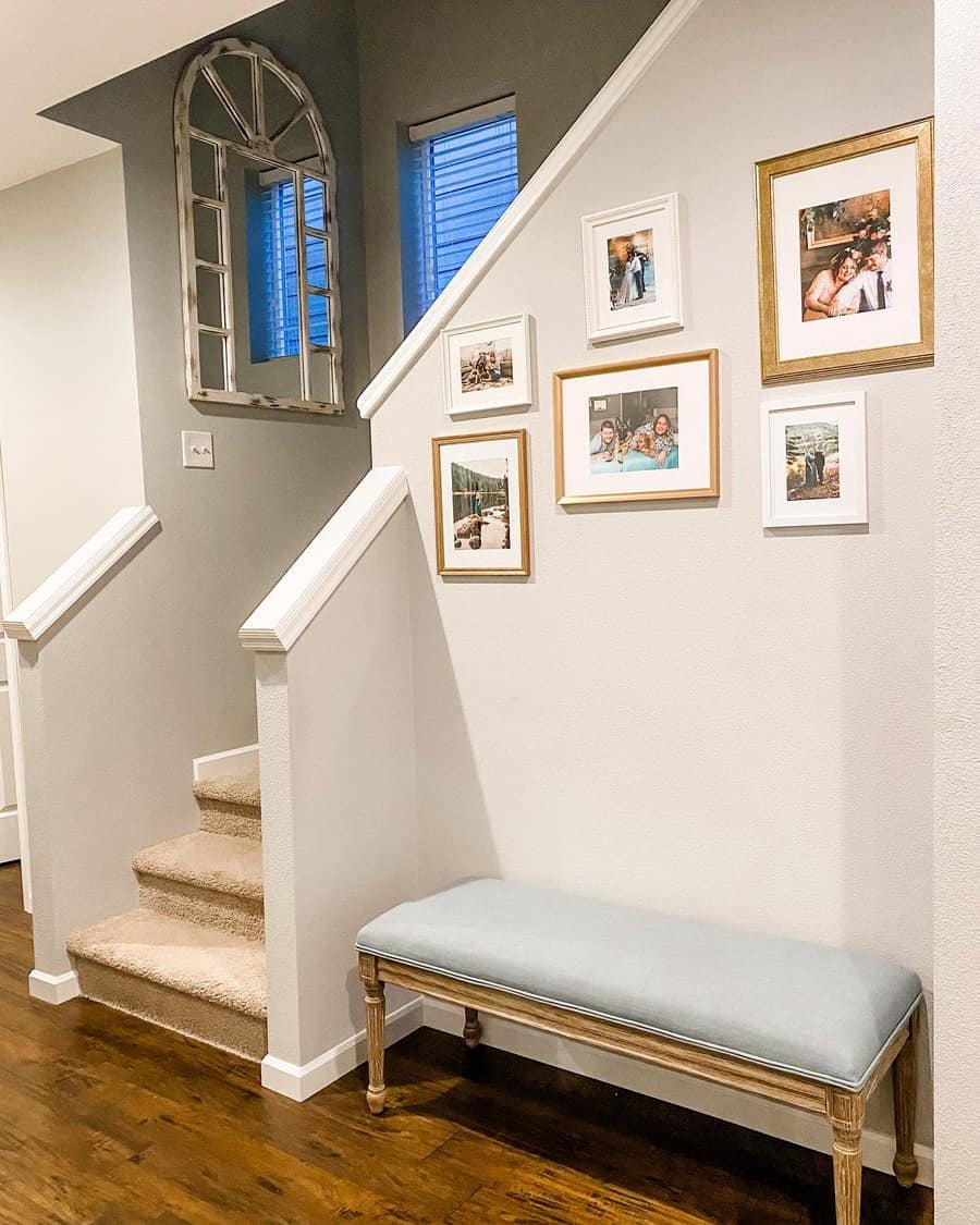 Hallway with a staircase, gallery wall of framed photos, and a bench with a light blue cushion on a wooden floor