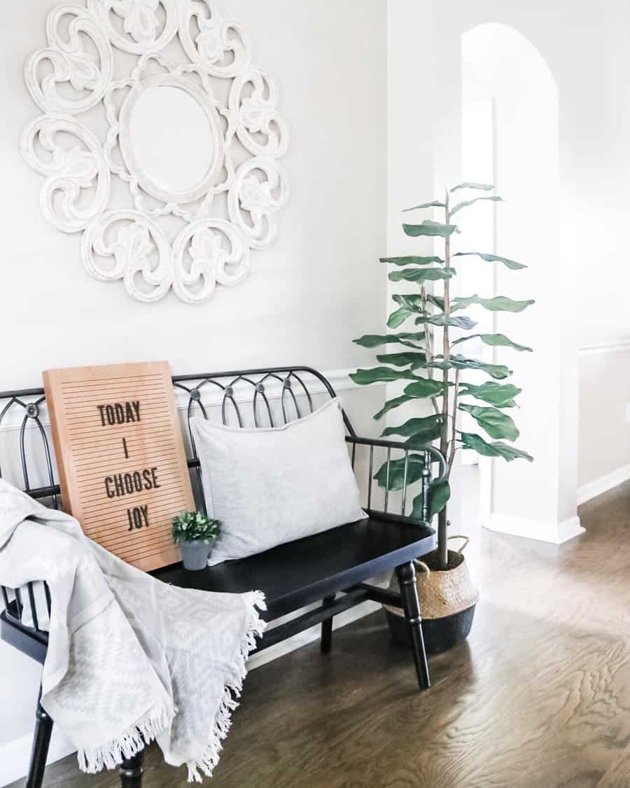 Bright and inviting entryway with a black metal bench, soft neutral decor, a statement wall mirror, and greenery for a cozy, welcoming feel