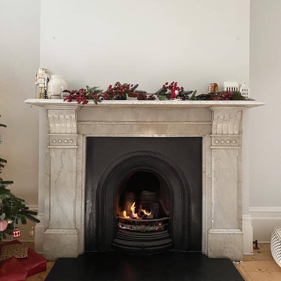 A classic marble fireplace with a festive garland, decorated with Christmas accents, and a warm fire glowing, creating a cozy holiday atmosphere