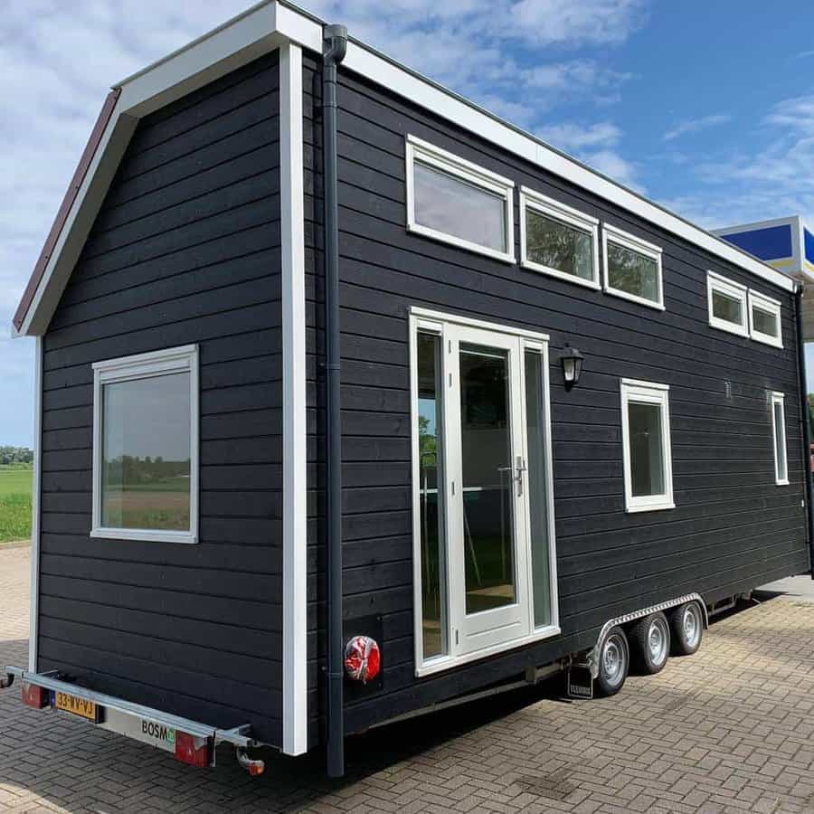 A black tiny house on wheels with multiple windows and a door