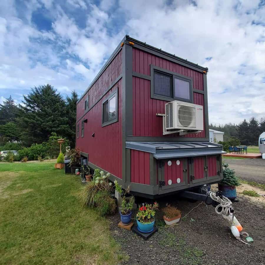 A red and gray tiny house on wheels with plants outside