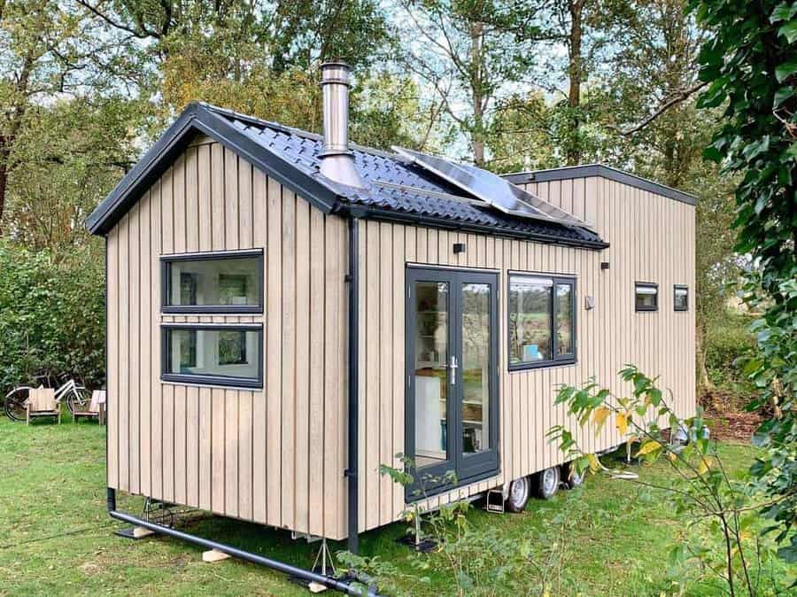 A cozy tiny house with wood siding and black trim in a forested area