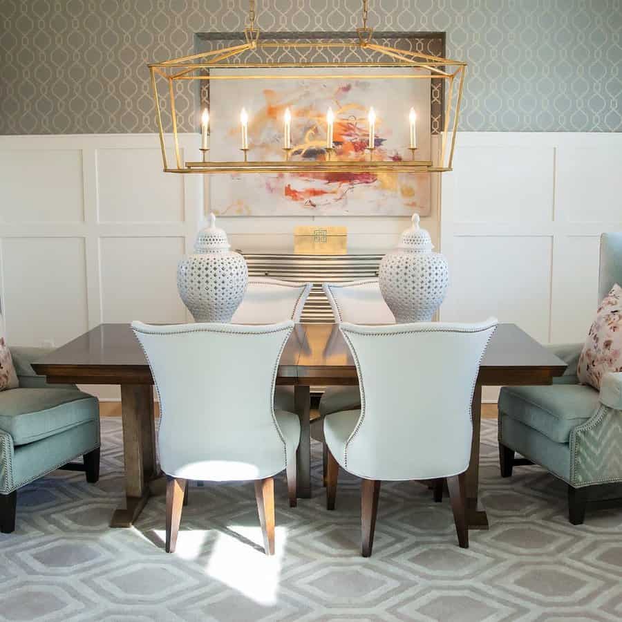 Elegant dining room with a wooden table, white chairs, light blue armchairs, large white vases, and a gold chandelier