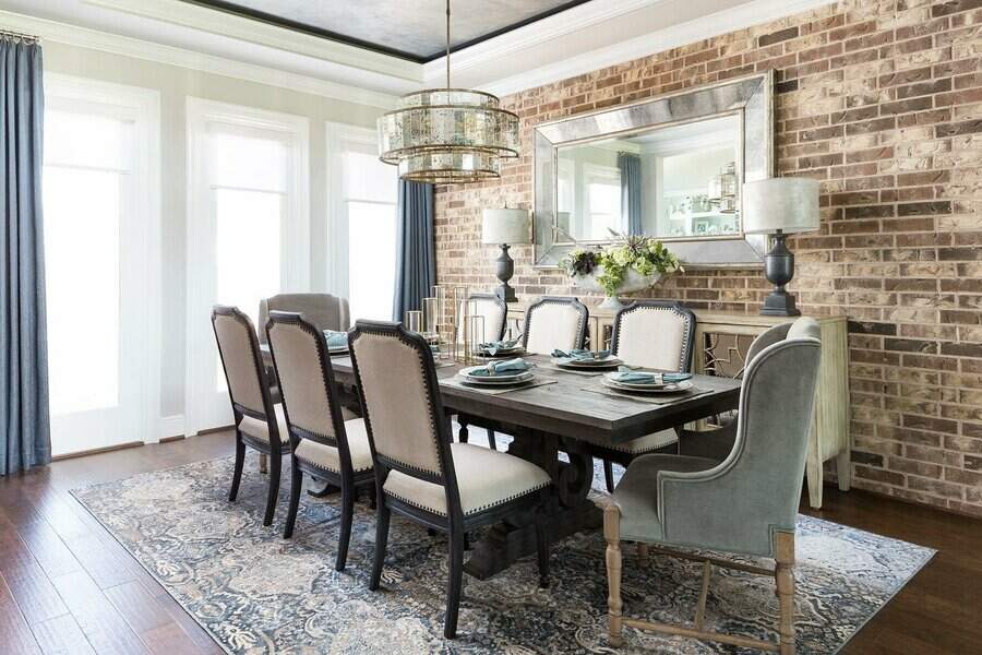 Elegant dining room with a wooden table, cushioned chairs, brick wall, large mirror, chandelier, and decorative table setting