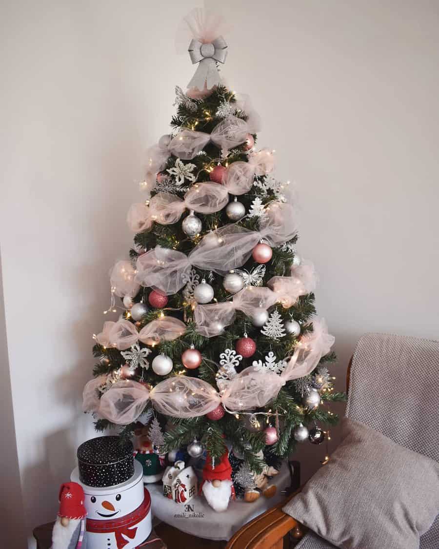 Christmas tree decorated with lights, ornaments, and white garland next to a snowman