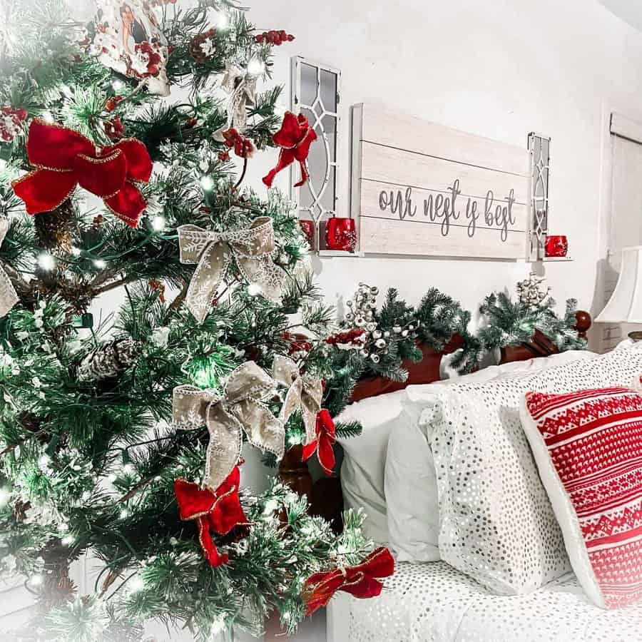 Festive bedroom with a Christmas tree adorned with red and gold bows, next to a bed with red and white pillows and decor