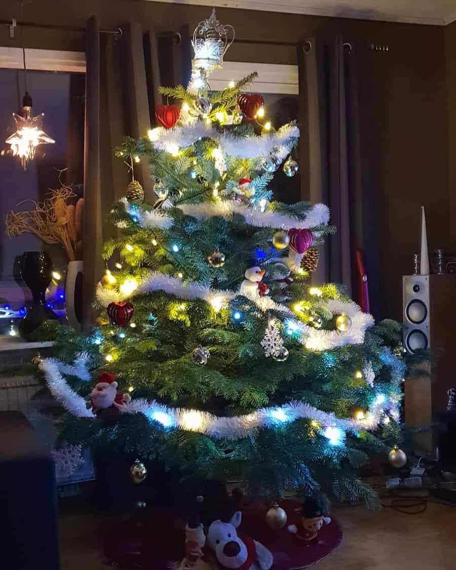 Decorated Christmas tree with white garlands, red and gold ornaments, and glowing lights in a cozy room with speakers and star lamp