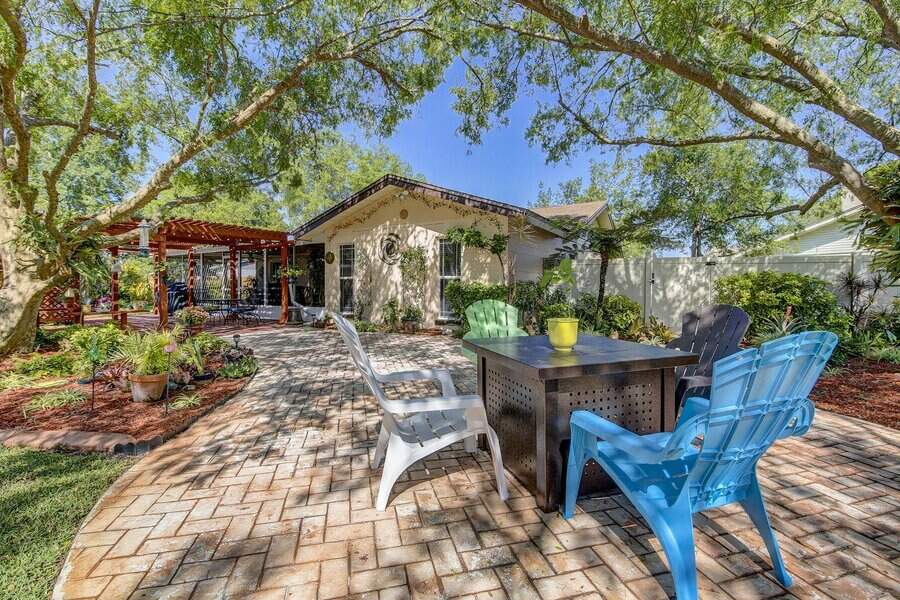 Sunny backyard with patio furniture under trees, brick patio, and pergola in the background