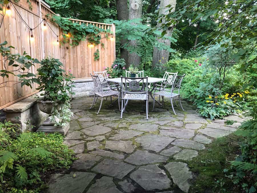 Cozy garden patio with a round metal table, four chairs, string lights, and lush greenery