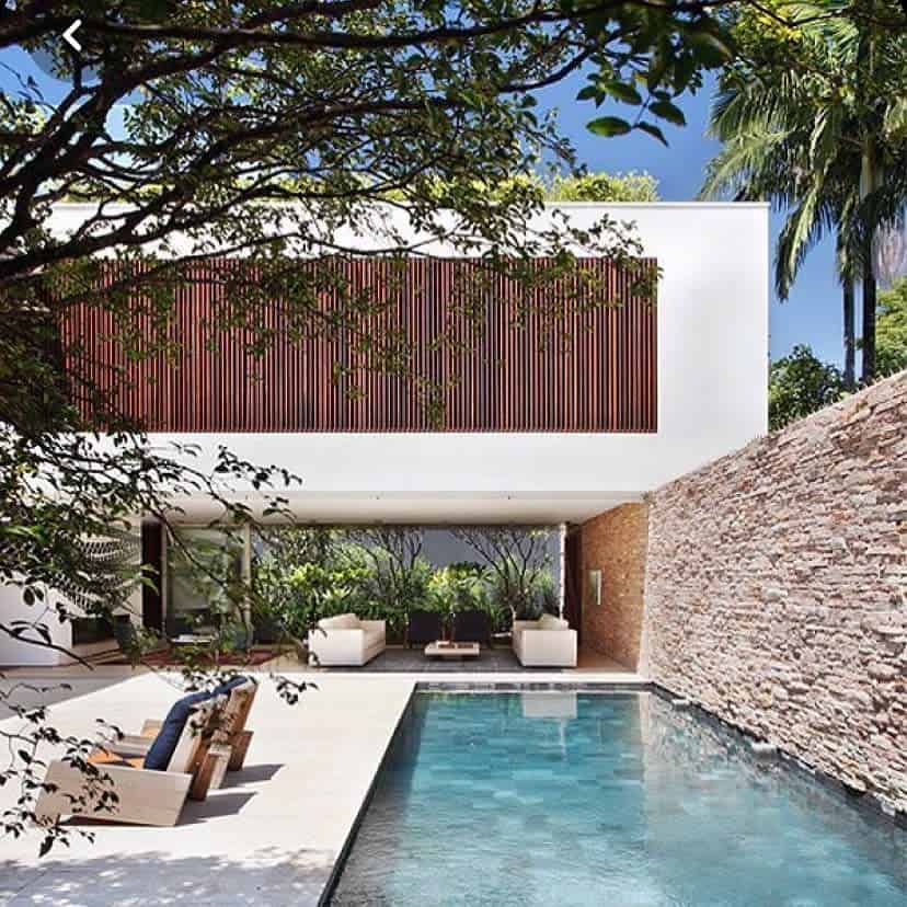 Modern backyard pool with sleek stone walls, lush greenery, and open-concept lounge space, creating a serene tropical retreat