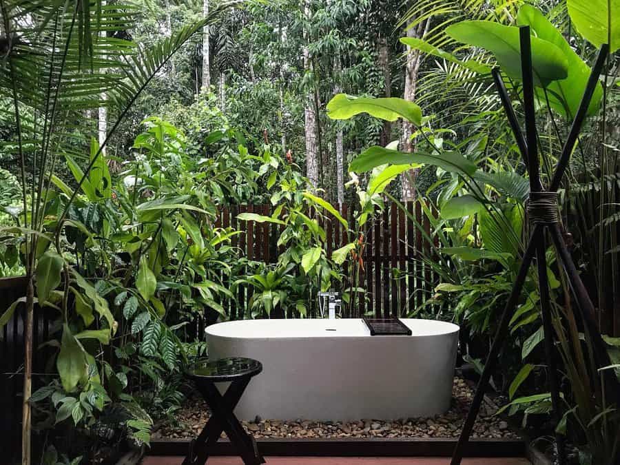 Outdoor bathtub surrounded by lush tropical plants and trees, creating a serene and natural atmosphere