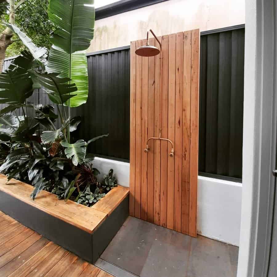 Outdoor shower with wooden paneling, surrounded by lush green plants, on a wooden deck