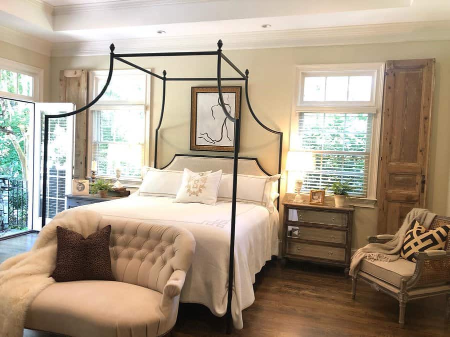 Elegant canopy bed with a curved black metal frame, crisp white bedding, and a tufted bench, creating a classic and sophisticated bedroom retreat