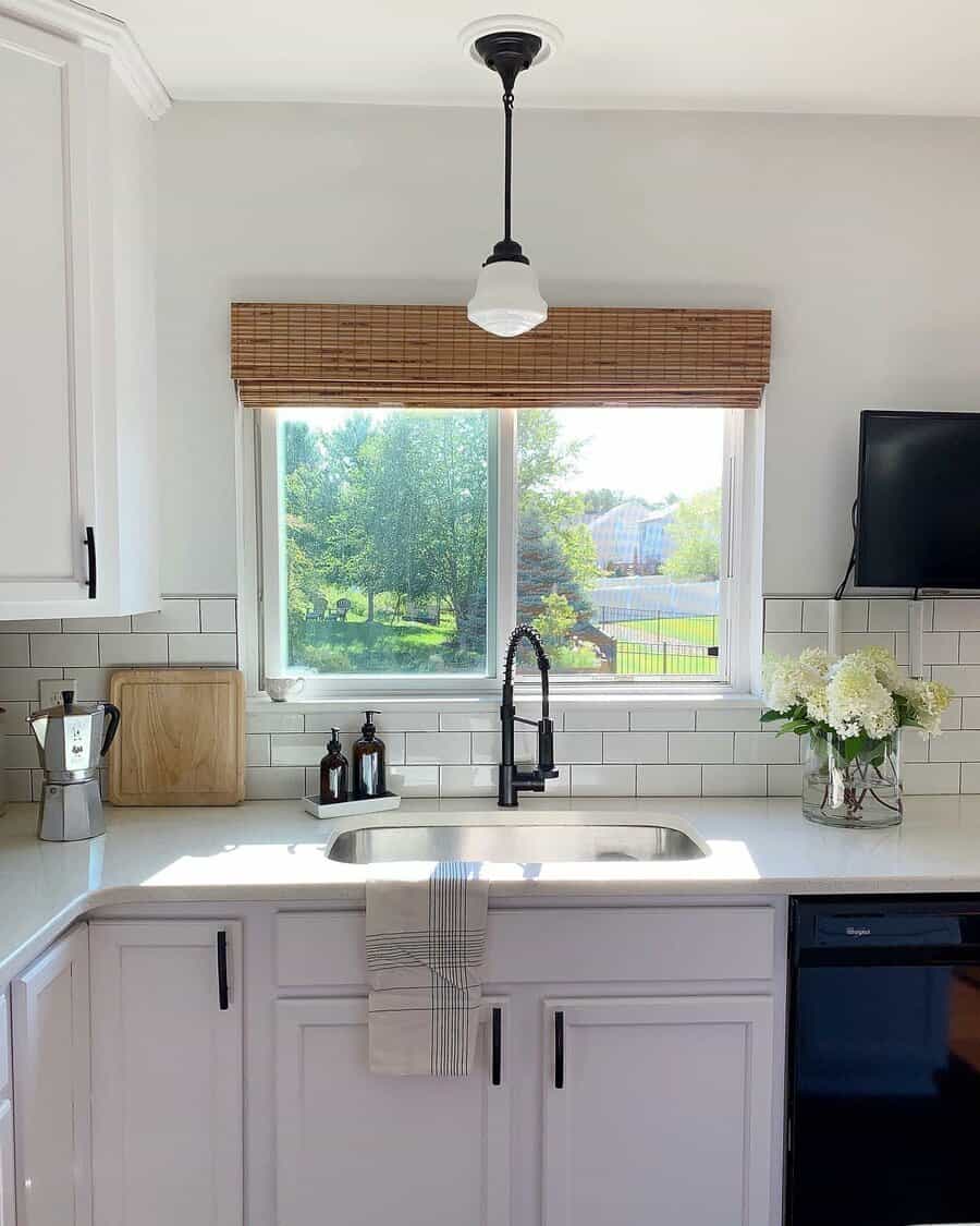 Bright farmhouse kitchen with an undermount stainless steel sink, black pull-down faucet, white subway tile backsplash, and a warm bamboo window shade