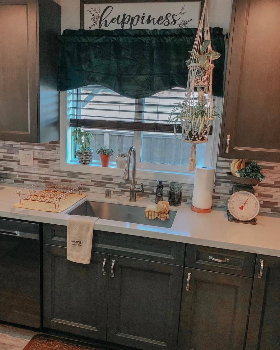 Cozy kitchen with a deep undermount sink, high-arch faucet, dark cabinetry, mosaic tile backsplash, and hanging greenery for a warm, rustic feel