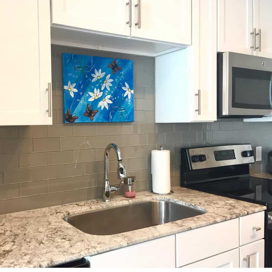 Modern kitchen with marble countertop, stainless steel undermount sink, stove, and microwave; a colorful floral painting decorates the backsplash