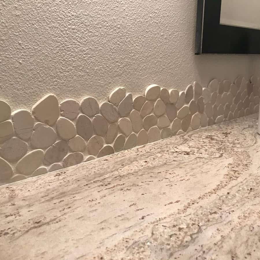 Nature-inspired bathroom with pebble stone backsplash and textured beige wall, paired with a light granite countertop for an organic feel.