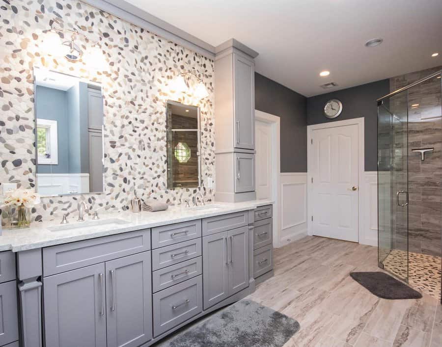 Spacious bathroom with pebble mosaic backsplash, double vanity in soft gray, marble countertops, and a glass walk-in shower for a spa-like feel.