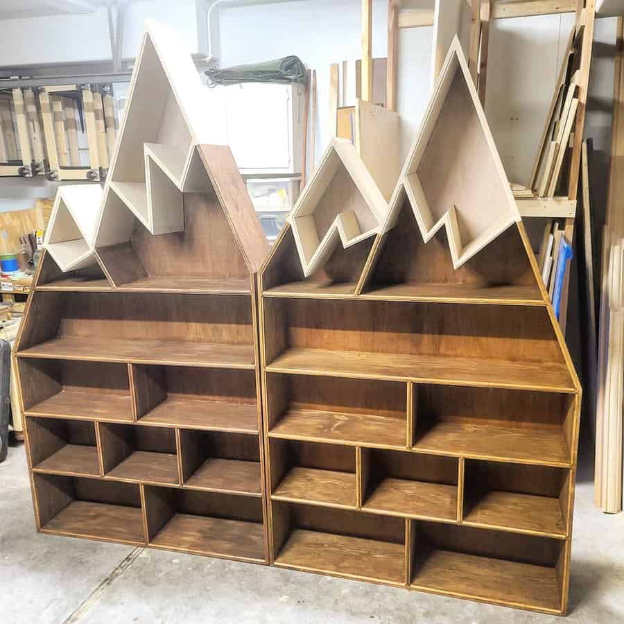 Handcrafted mountain-shaped wooden bookshelves with unique geometric peaks, featuring multiple storage compartments in a woodworking shop.