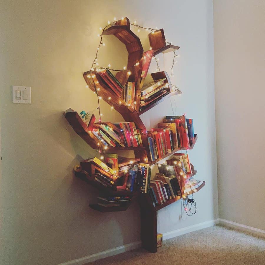 Whimsical tree-shaped bookshelf mounted on a wall, filled with colorful books and decorated with warm fairy lights for a cozy ambiance.