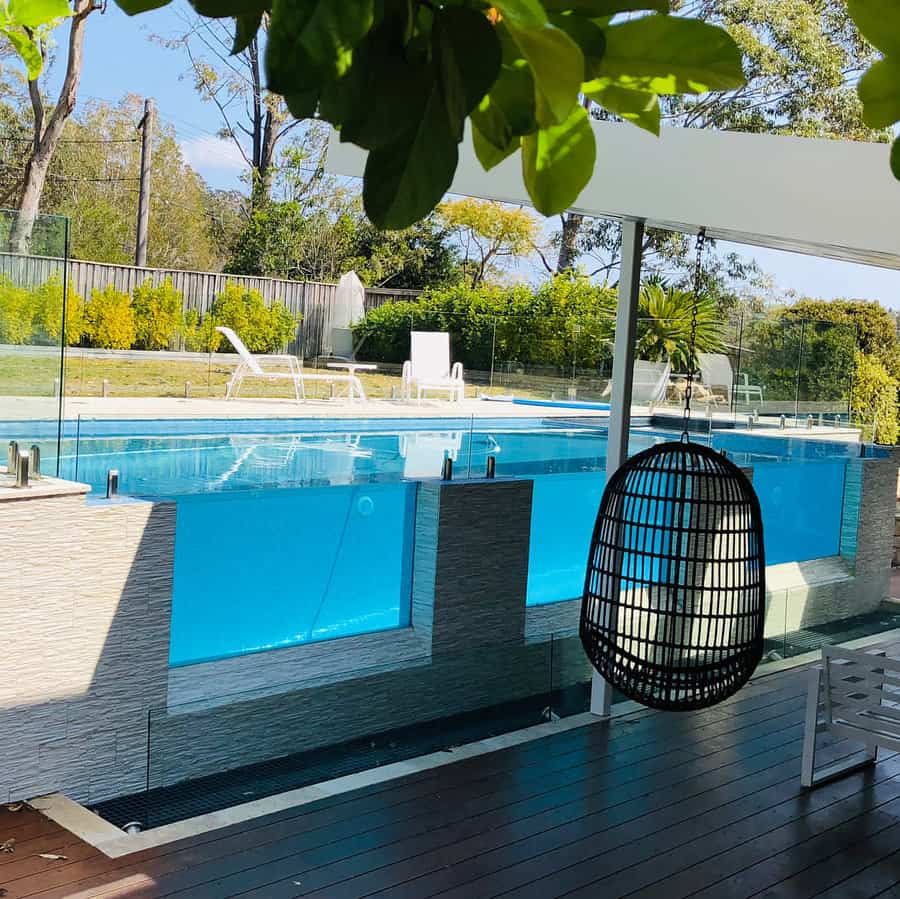 Elegant above-ground pool with glass panel walls, sleek tiling, and a cozy hanging chair for a luxurious outdoor retreat