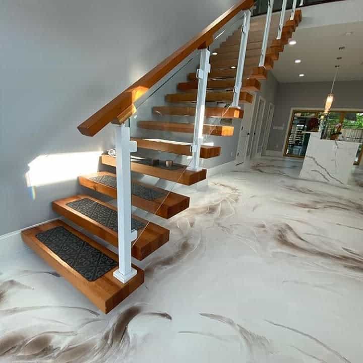 Wooden staircase with white railing, modern design; marbled floor with brown swirls; bright lighting from above