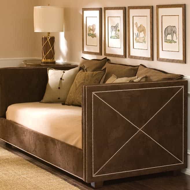 Brown daybed with beige cushions against a wall displaying four framed animal sketches, next to a lamp on a wooden floor