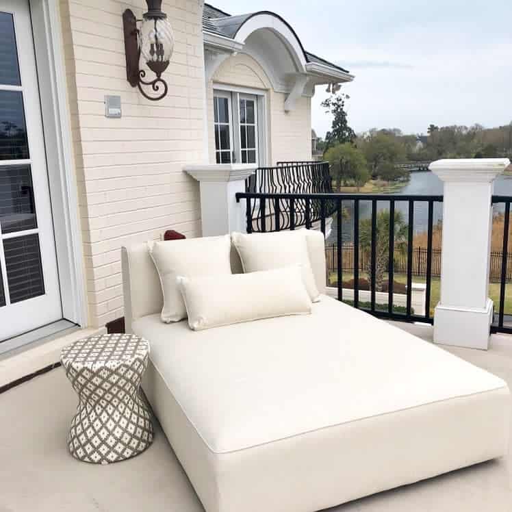 Luxurious cream upholstered daybed on a balcony with plush pillows and a patterned side table, offering a serene spot with stunning lake views