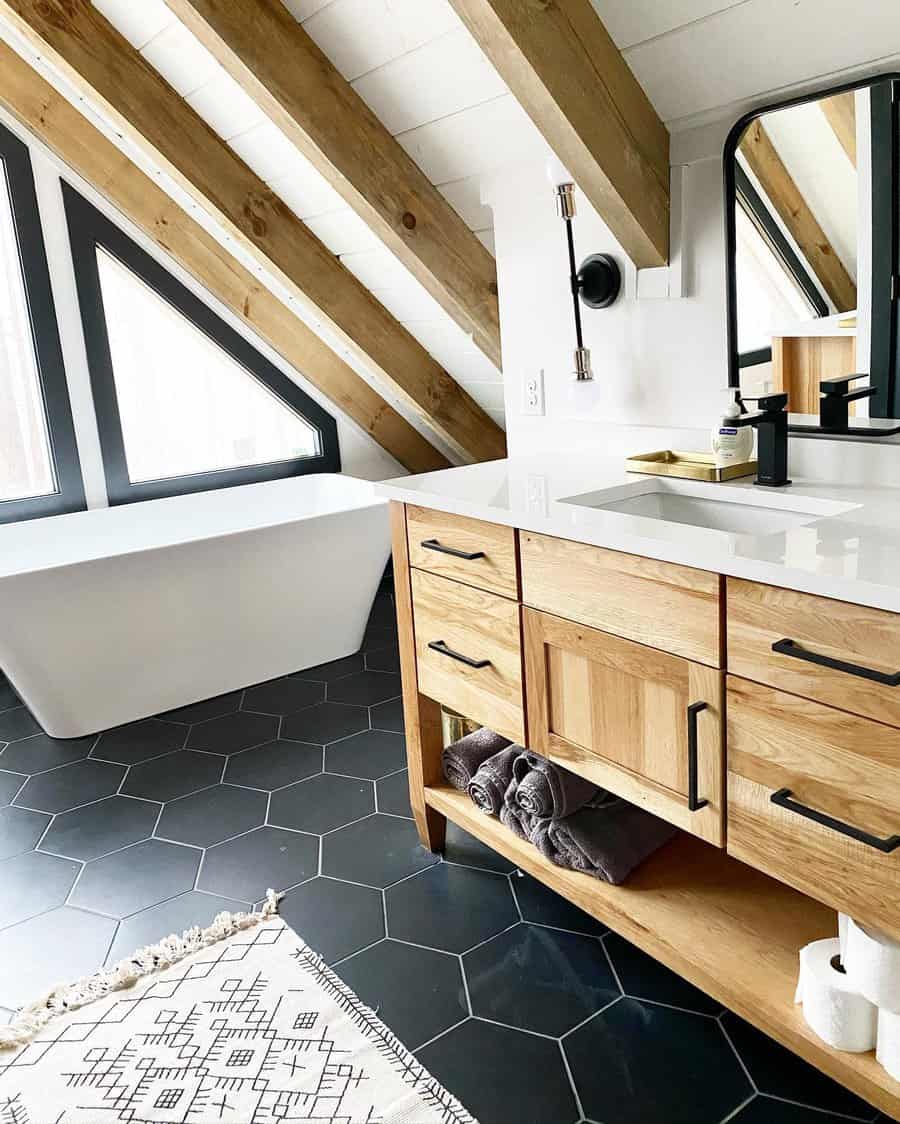 Rustic-modern bathroom with a vaulted ceiling, exposed wooden beams, and black hexagonal flooring, creating a cozy yet contemporary retreat.