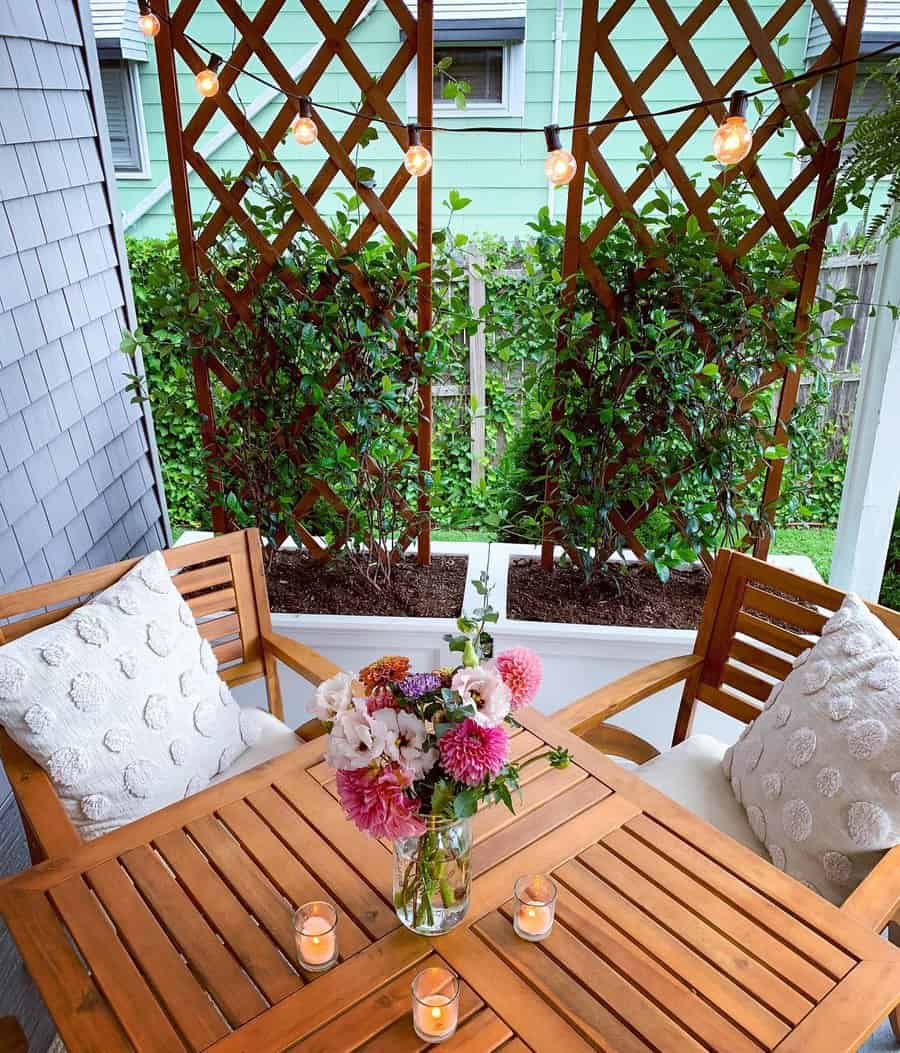 Cozy patio with a wooden trellis privacy screen, climbing greenery, string lights, and a warm dining setup with candles and fresh flowers