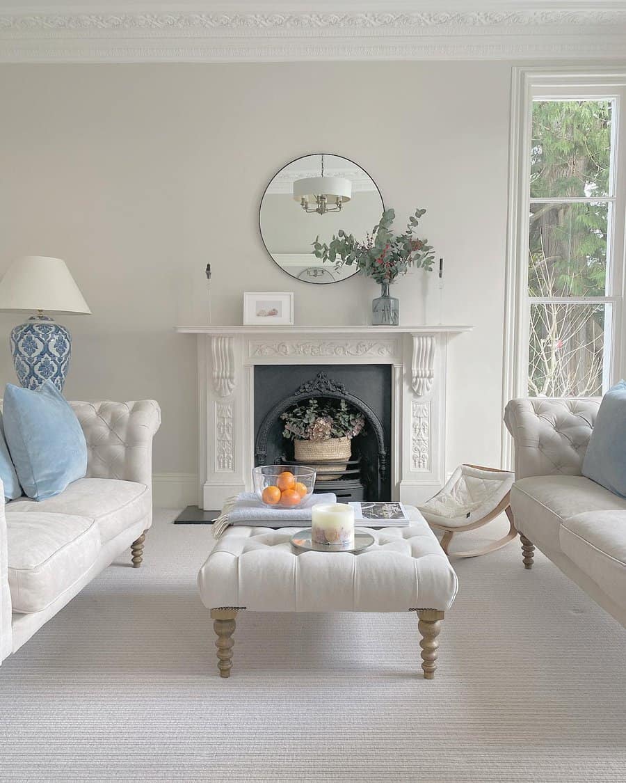 A refined Victorian-style fireplace with intricate detailing, complemented by a circular mirror above and soft, neutral-colored furniture, creating a calm and elegant atmosphere