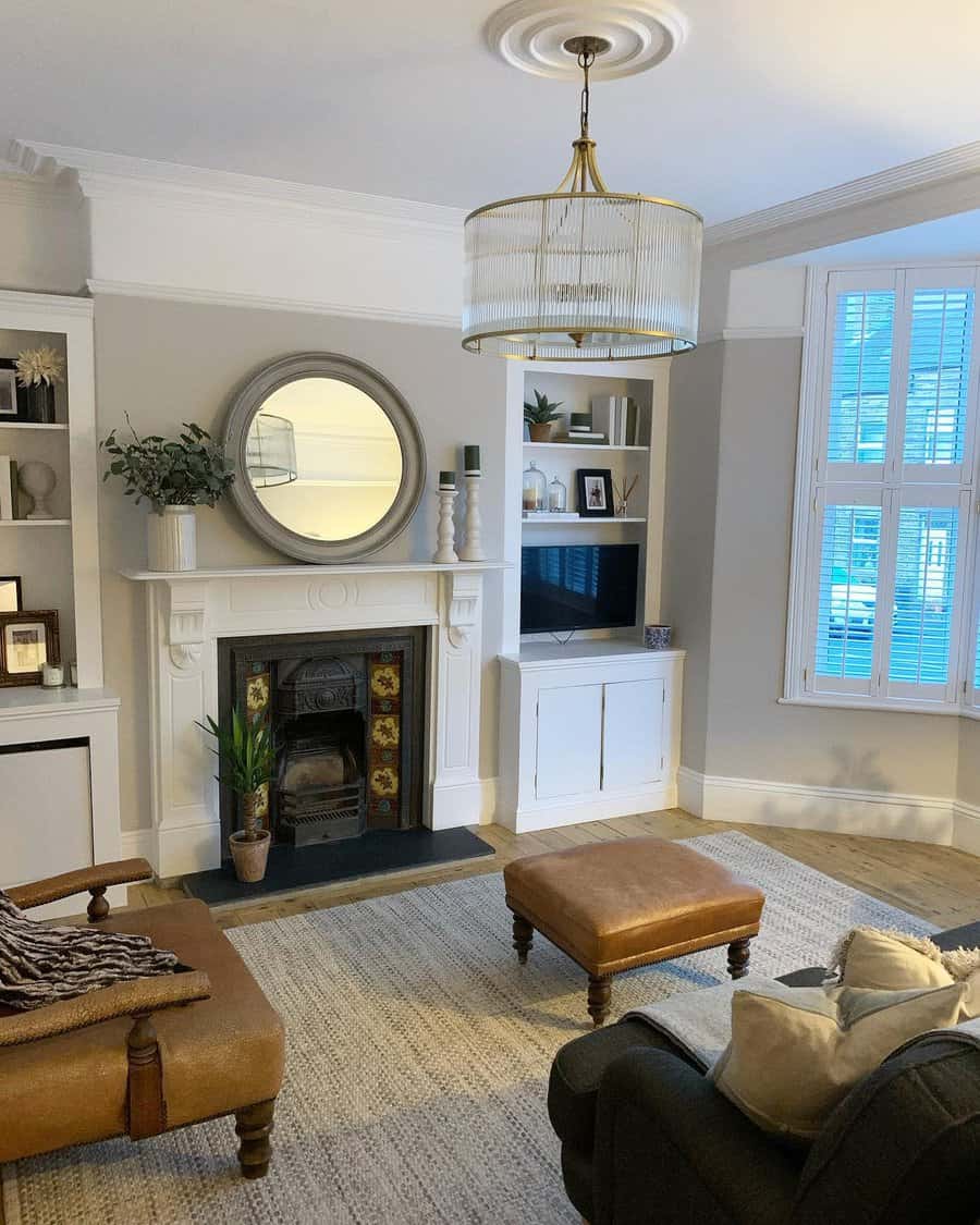 A classic Victorian fireplace with ornate details, framed by a large circular mirror above and a cozy, modern living room setup with comfortable seating and a TV