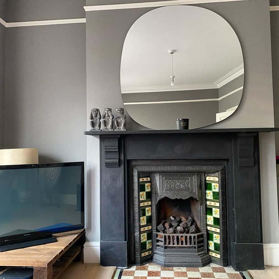 A striking black Victorian fireplace with intricate detailing, complemented by a large, modern oval mirror above and stylish decor, creating a bold, elegant look