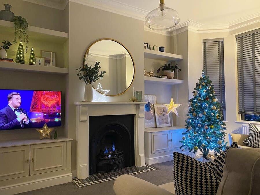 A cozy Victorian-style fireplace with a black insert, framed by a circular mirror above and festive decor, including a Christmas tree, creating a warm, inviting atmosphere