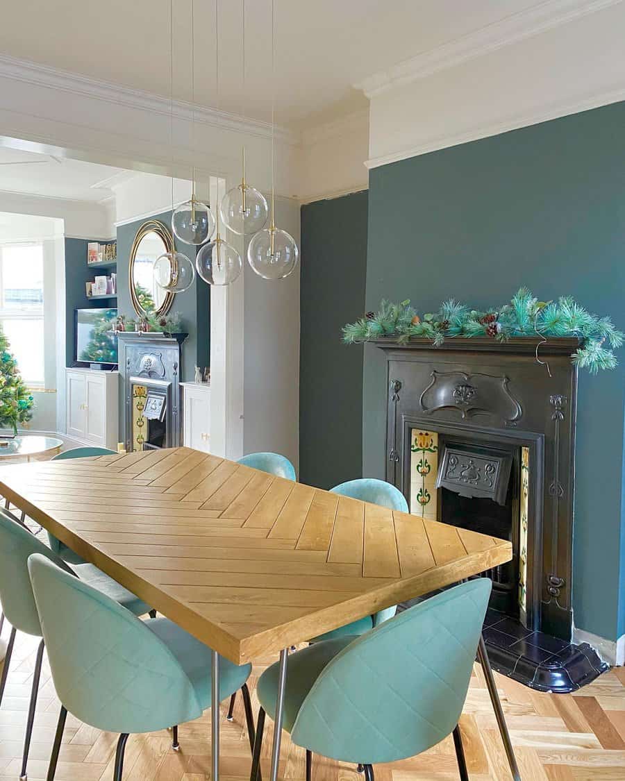 A cozy Victorian fireplace with green garland and festive decor, framed by vintage tiles, and complemented by a modern dining table and pendant lights, creating a stylish and welcoming living space